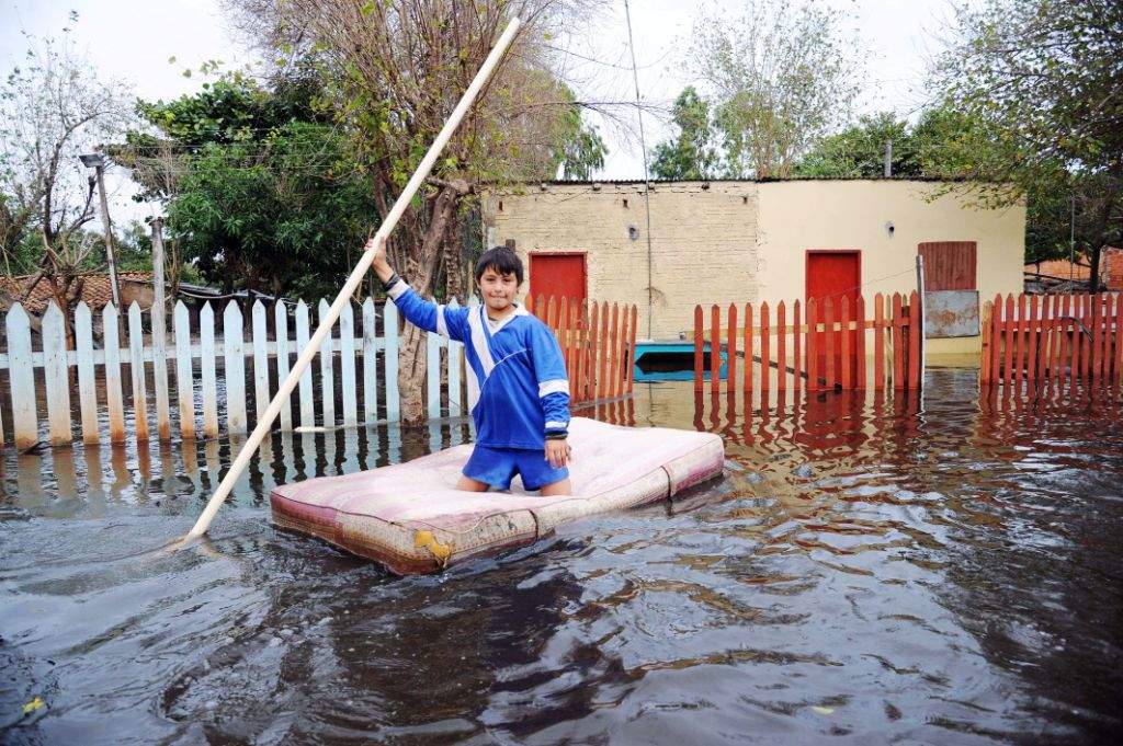 A child navigates on a makeshift raft in a flooded neighborhood of Asuncion. (AFP PHOTO/NORBERTO Duarte) 