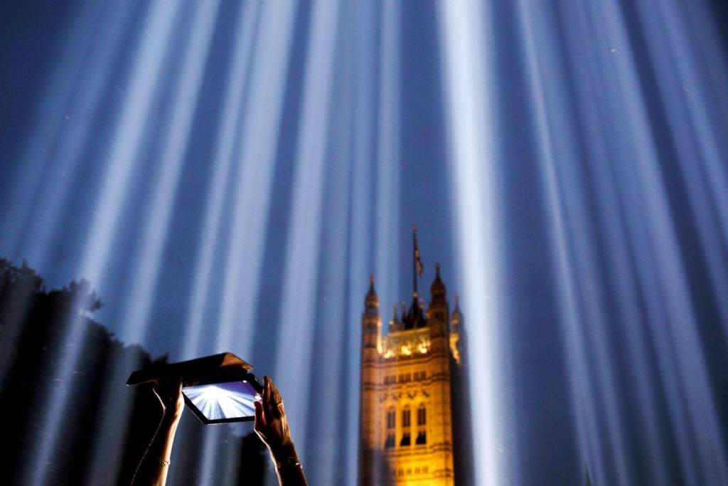 A woman uses a tablet to photograph shafts of light piercing the night sky at an installation entitled 'Spectra' by Japanese artist Ryoji Ikeda located at Victoria Tower Gardens adjacent to the Houses of Parliament, partially visible in background, in London. (AP Photo/David Azia)