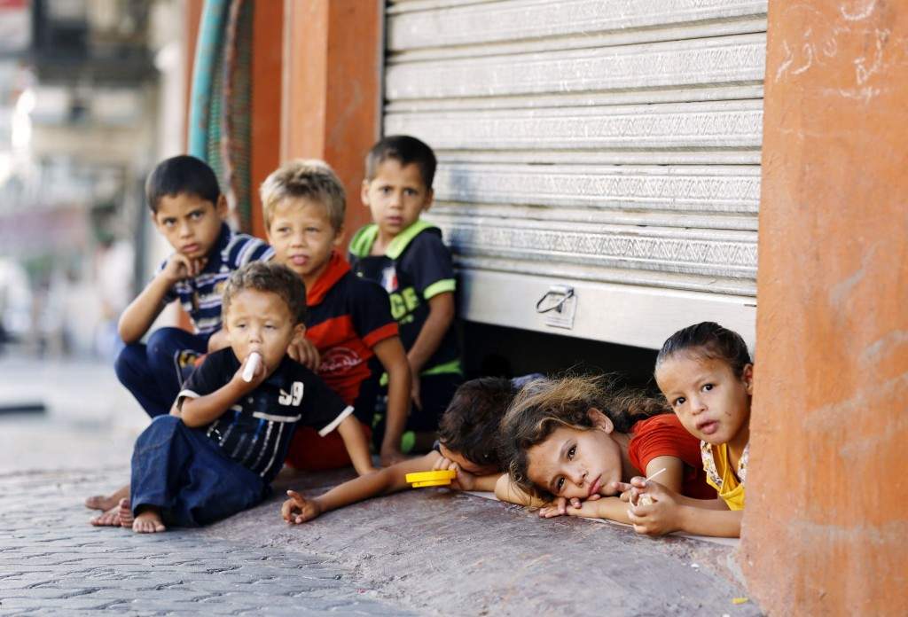 Displaced Palestinian children peak from under a shop door, where their family is taking shelter in Gaza City. (AFP PHOTO / MOHAMMED ABED)