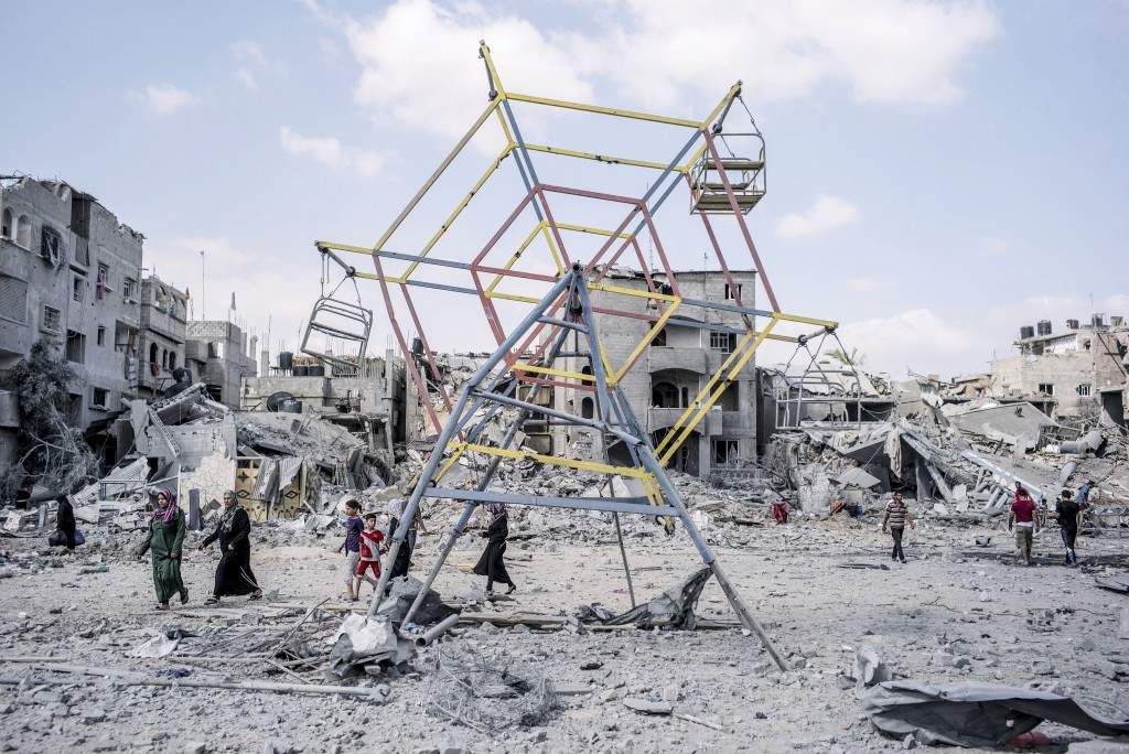 Palestinians go their way past rubbles and a mini ferris wheel in the northern district of Beit Hanun in the Gaza Strip. (AFP PHOTO/MARCO LONGARI)