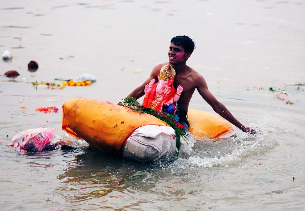 A devotee carries an idol of the Lord Ganesh on a makeshift raft into the Sabarmati river. (REUTERS/Amit Dave)