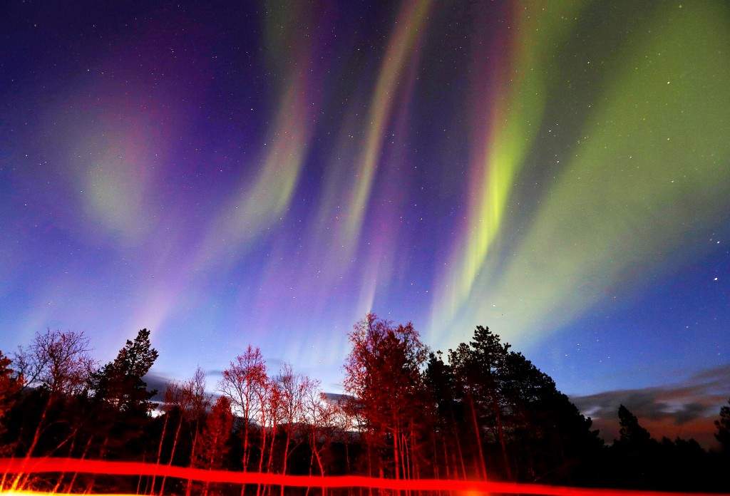 Vehicles drive by as a display of Aurora Borealis (Northern Lights) is seen north of the Arctic Circle, over the village of Mestervik in northern Norway