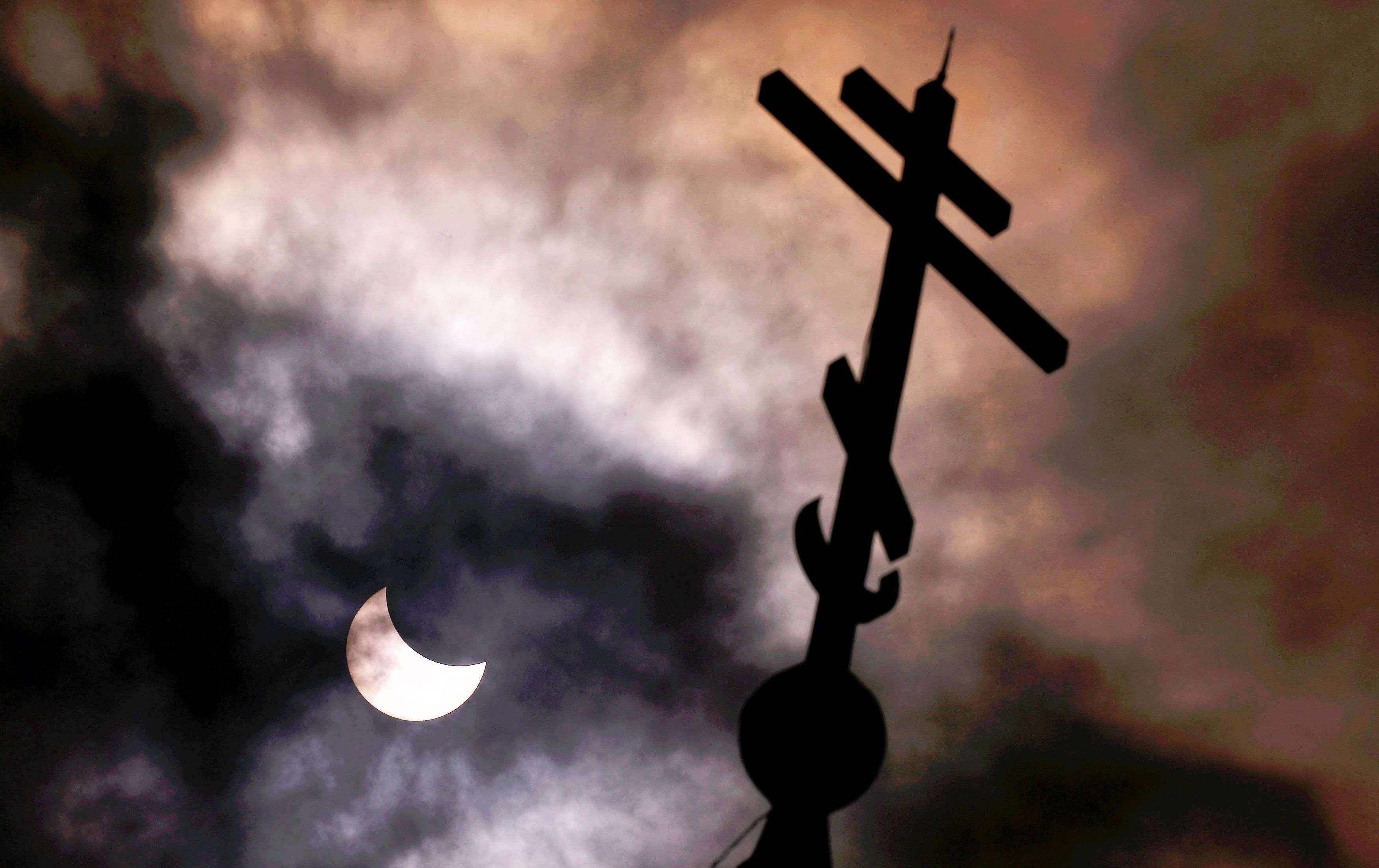 A partial solar eclipse forms in the sky through clouds near the cross of the Church of St Nicholas the Miracle-Maker in Sofia. (REUTERS/Stoyan Nenov)