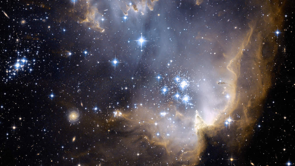 NGC 602: Bright, blue, newly formed stars are blowing a cavity in the center of a star-forming region in the Small Magellanic Cloud. At the heart of the star-forming region lies star cluster NGC 602. High-energy radiation blazing out from the young stars sculpts the inner edge of the outer portions of the nebula, slowly eroding it away and eating into the material beyond. (Courtesy: http://hubblesite.org/)