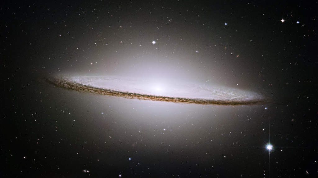 Sombrero Galaxy: This is a spiral galaxy seen nearly edge-on. The dark band across the center is the result of material in the flat disk of the galaxy obscuring the light of stars and gas behind it. The glowing bulge holds a population of stars largely different from those in the flat disk. Look close to see numerous globular clusters, which appear as slightly fuzzy stars, each of which is itself composed of many hundreds of thousands of stars.  (Courtesy: http://hubblesite.org/)