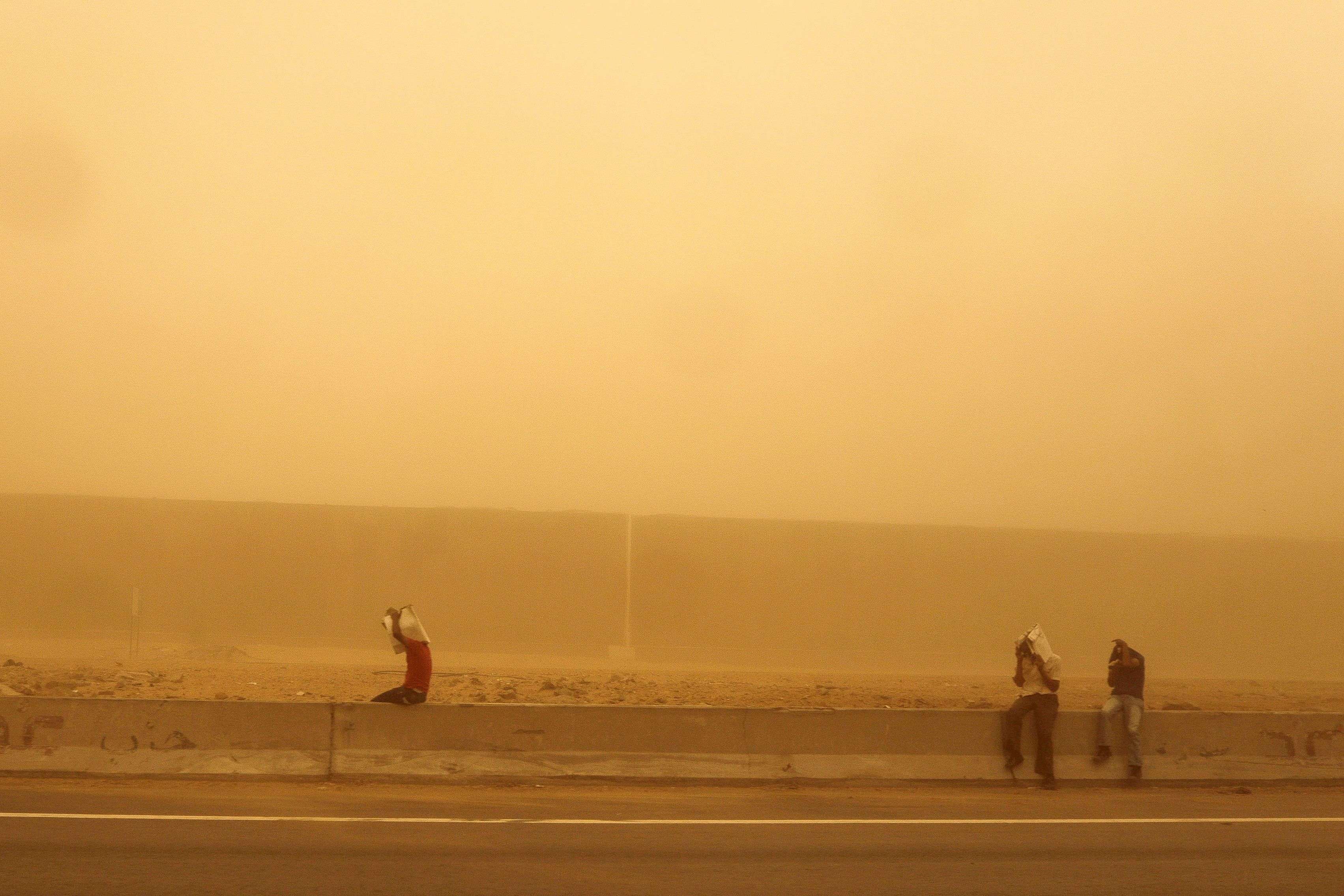 Men cover their faces during a sandstorm and a heat wave as they wait for transportation on a highway in Cairo, Egypt.(AP/Mosa'ab Elshamy) 