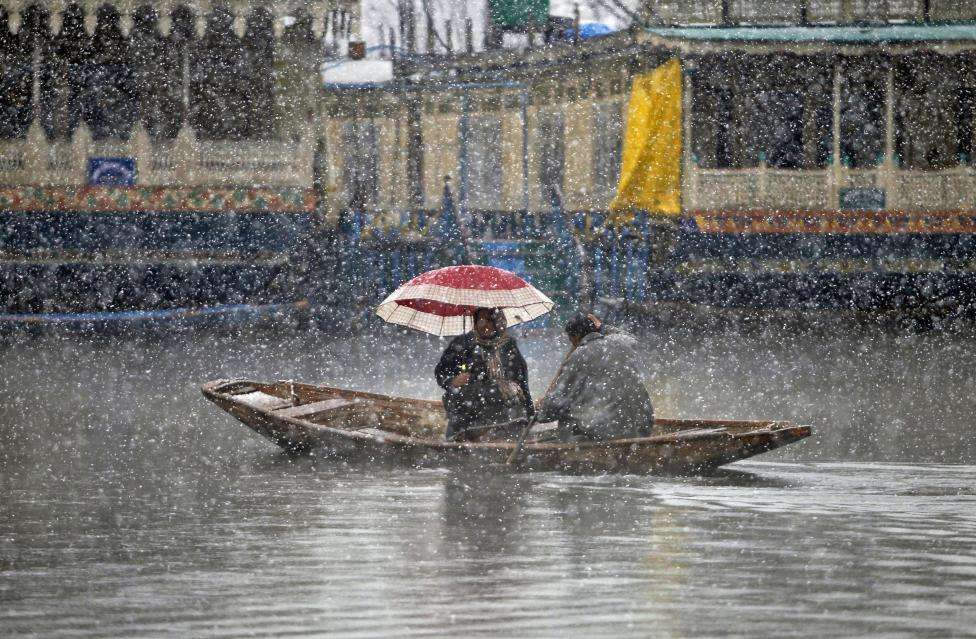 A man rows a boat on the Dal Lake as a woman holds an umbrella during snowfall in Srinagar. (REUTERS/Danish Ismail/Files)