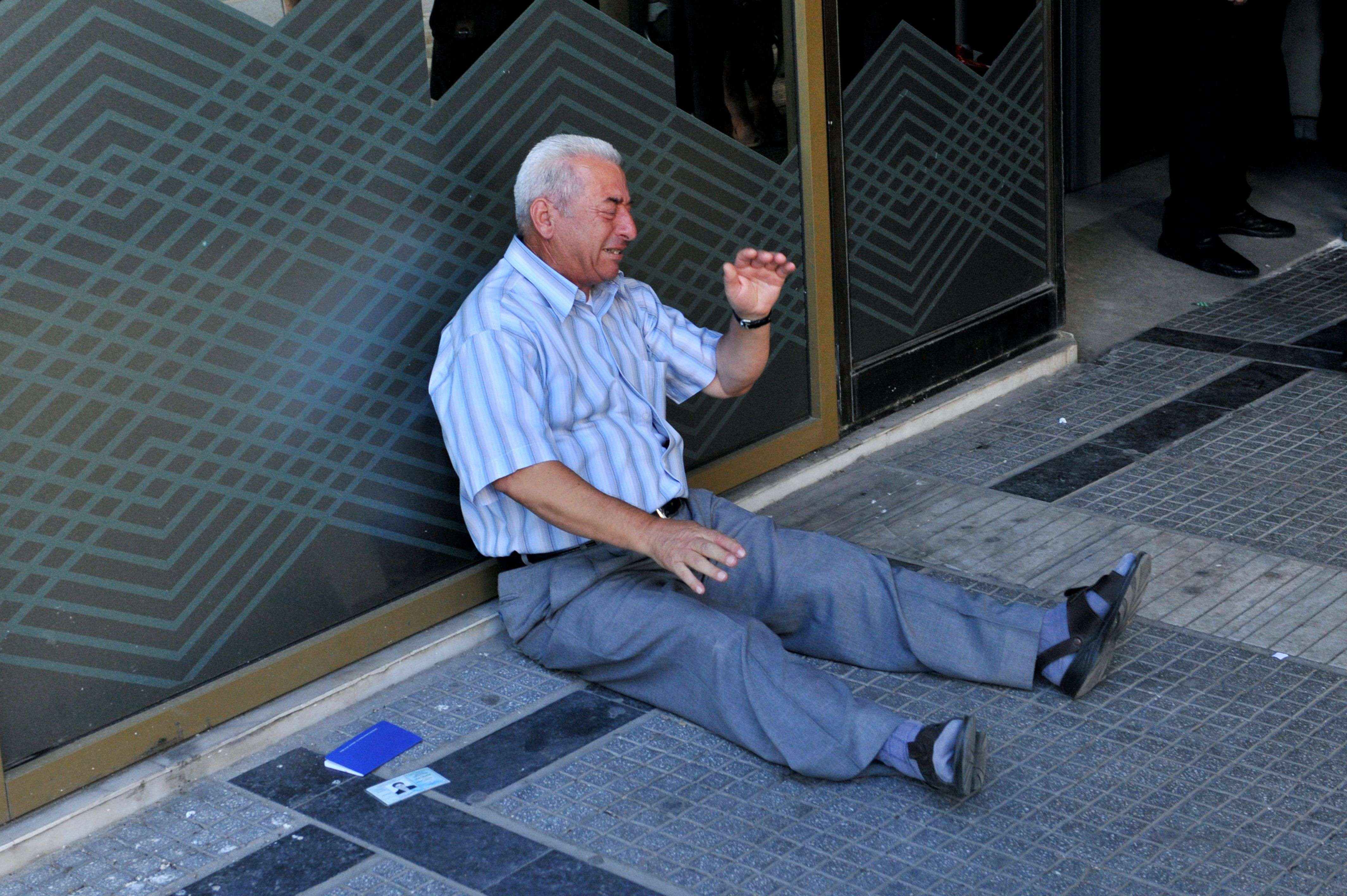 A distressed pensioner sits on the ground outside a national bank branch, as banks opened only for pensioners to allow them to withdraw their pensions, with a limit of 120 euros, in Thessaloniki. Greece is almost evenly split over a crucial weekend referendum that could decide its financial fate, with a 'Yes' result possibly ahead by a whisker, the latest survey Friday showed. Prime Minister Alexis Tsipras's government is asking Greece's voters to vote 'No' to a technically phrased question asking if they are willing to accept more tough austerity conditions from international creditors in exchange for bailout funds. (AFP PHOTO /SAKIS MITROLIDIS)