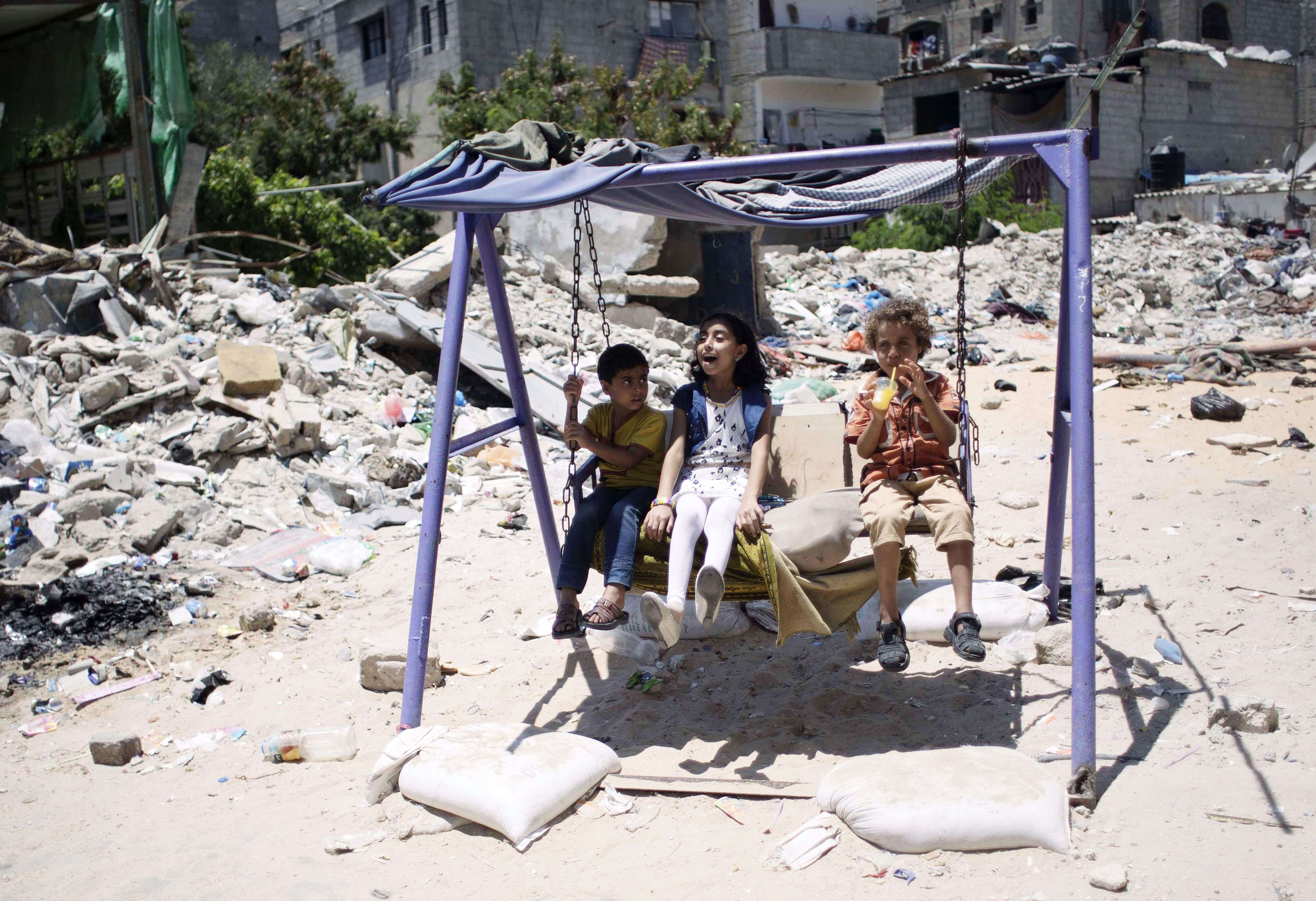Palestinian children play on a swing near the rubble of buildings, reportedly destroyed during the 50-day war between Israel and Hamas militants in the summer of 2014, in the southern Gaza Strip town of Rafah, on the second day of Eid al-Fitr holiday which marks the end of the Muslim holy month of Ramadan. (AFP/ Said Khatib)