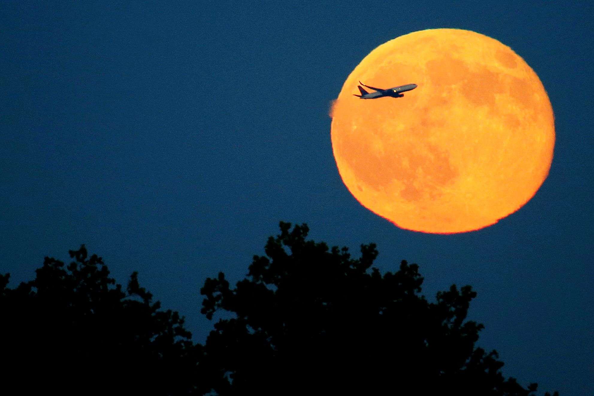 A plane ascends in front of a blue moon rising seen from Liberty State Park in Jersey City, N.J., Friday, July 31, 2015. The blue moon happens when the moon rises in its full stage twice during the same month. (AP Photo/Julio Cortez)