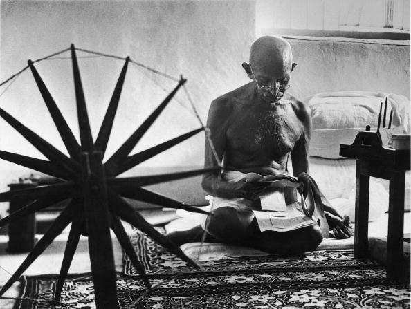 INDIA - 1946: Indian leader Mohandas Gandhi reading as he sits cross-legged on floor next to a spinning wheel which looms in the foreground as a symbol of India's struggle for Independence, at home. (Photo by Margaret Bourke-White/Time & Life Pictures/Getty Images)