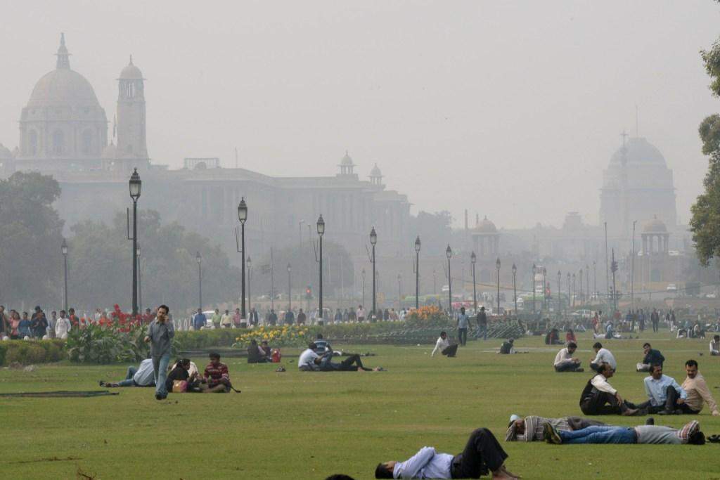 Indian people relax on the lawns near smog enveloped government offices on Rajpath in New Delhi on December 2, 2015.  AFP PHOTO/ Prakash SINGH