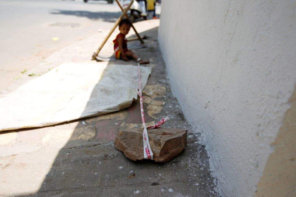 Barrier tape is tied around 15-month-old Shivani's ankle to prevent her from running away, while her mother Sarta Kalara works at a construction site nearby, in Ahmedabad, India, April 19, 2016. Kalara says she has no option but to tether her daughter Shivani to a stone despite her crying, while she and her husband work for 250 rupees ($3.8) each a shift digging holes for electricity cables in the city of Ahmedabad. There are about 40 million construction workers in India, at least one in five of them women, and the majority poor migrants who shift from site to site, building infrastructure for India's booming cities. Across the country it is not uncommon to see young children rolling in the sand and mud as their parents carry bricks or dig for new roads or luxury houses. REUTERS/Amit Dave       SEARCH "TIED TODDLER" FOR THIS STORY. SEARCH "THE WIDER IMAGE" FOR ALL STORIES