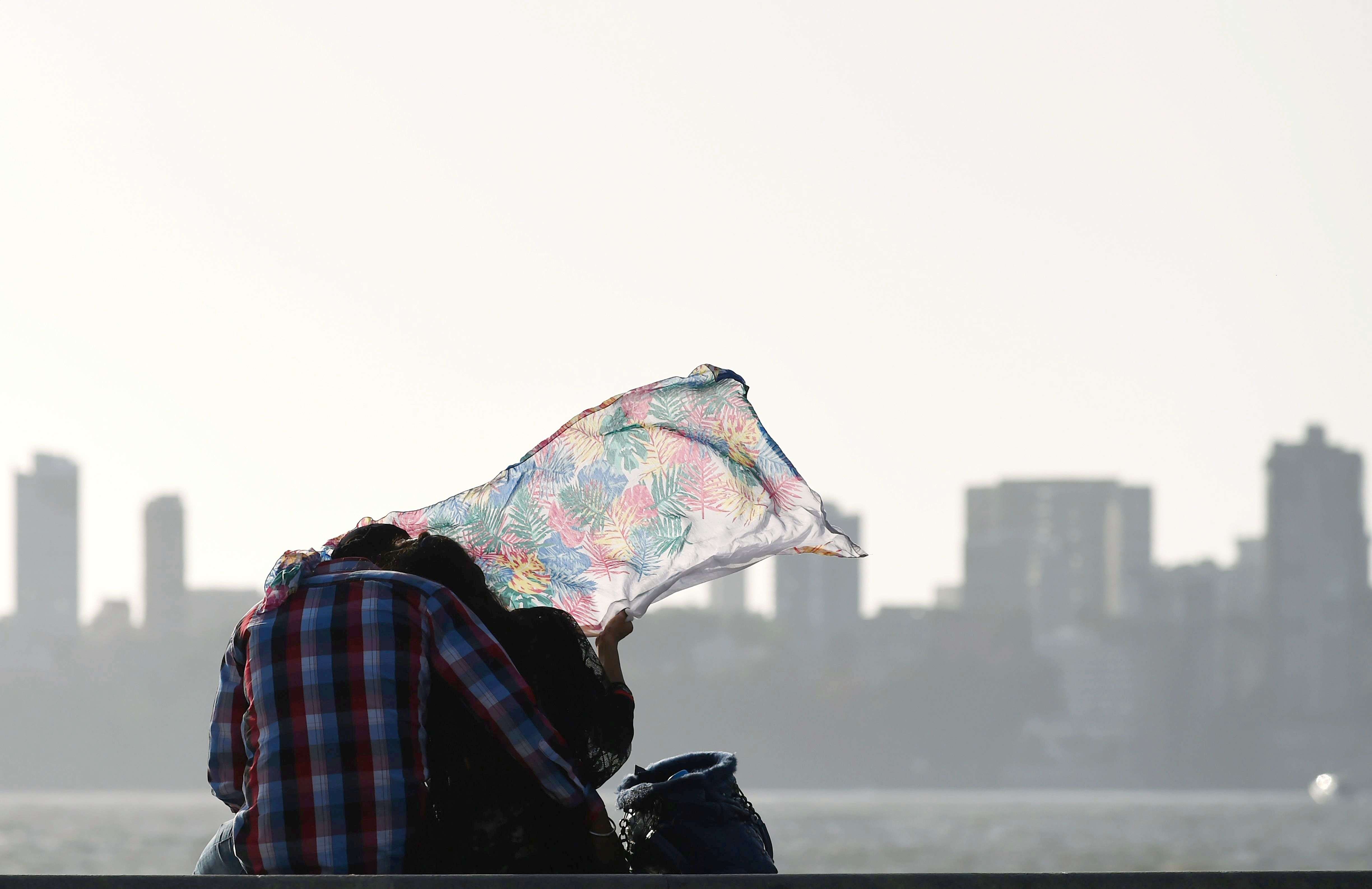A gust of wind blows the veil of an Indian woman as a couple watch the sunset on the Marine Drive promenade in Mumbai on May 31, 2016.  India is ranked 118th, according to The World Happiness Report 2016, published by the Sustainable Development Solutions Network (SDSN), a global initiative of the United Nations. Denmark took the top spot as the happiest country in the world, displacing Switzerland. The report said that India was among the group of 10 countries witnessing the biggest happiness declines, along with Venezuela, Saudi Arabia, Egypt, Yemen and Botswana. / AFP PHOTO / INDRANIL MUKHERJEE