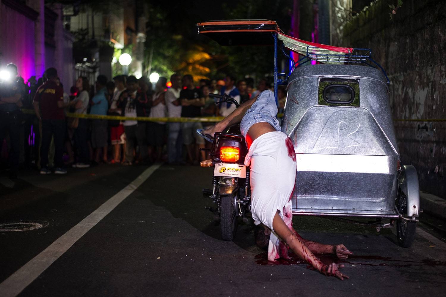 Bystanders watch the dead body of a tricycle driver shot by gunmen in Manila on July 22 (AFP / Noel Celis)