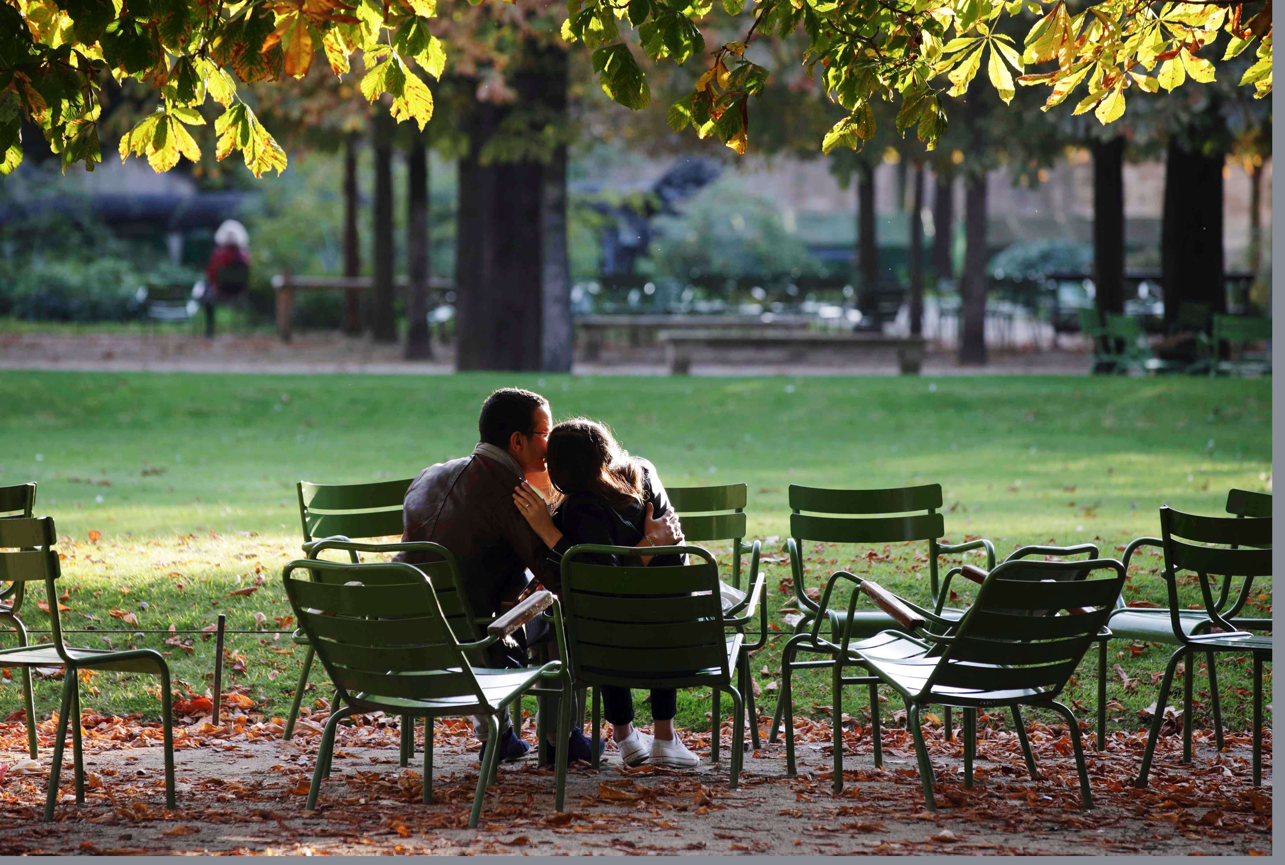 A couple kiss under trees with leaves that display autumn colors and mark the change of the season at the Tuileries Gardens in Paris, France