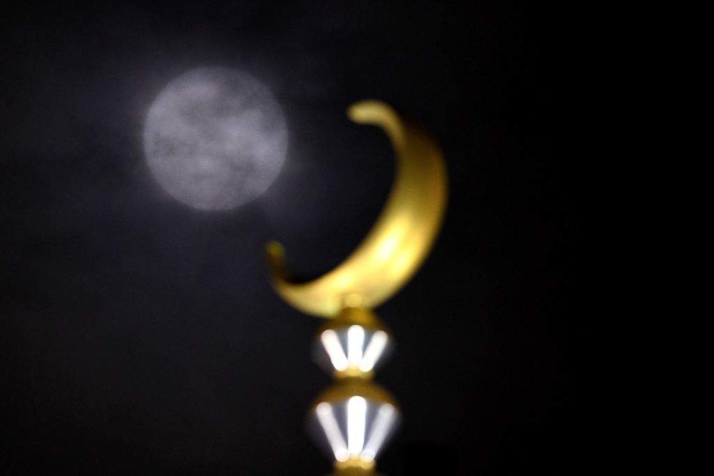 A 'supermoon' is seen obscured by clouds next to a crescent atop a mosque in Kuala Lumpur. (AFP PHOTO / MANAN VATSYAYANA)
