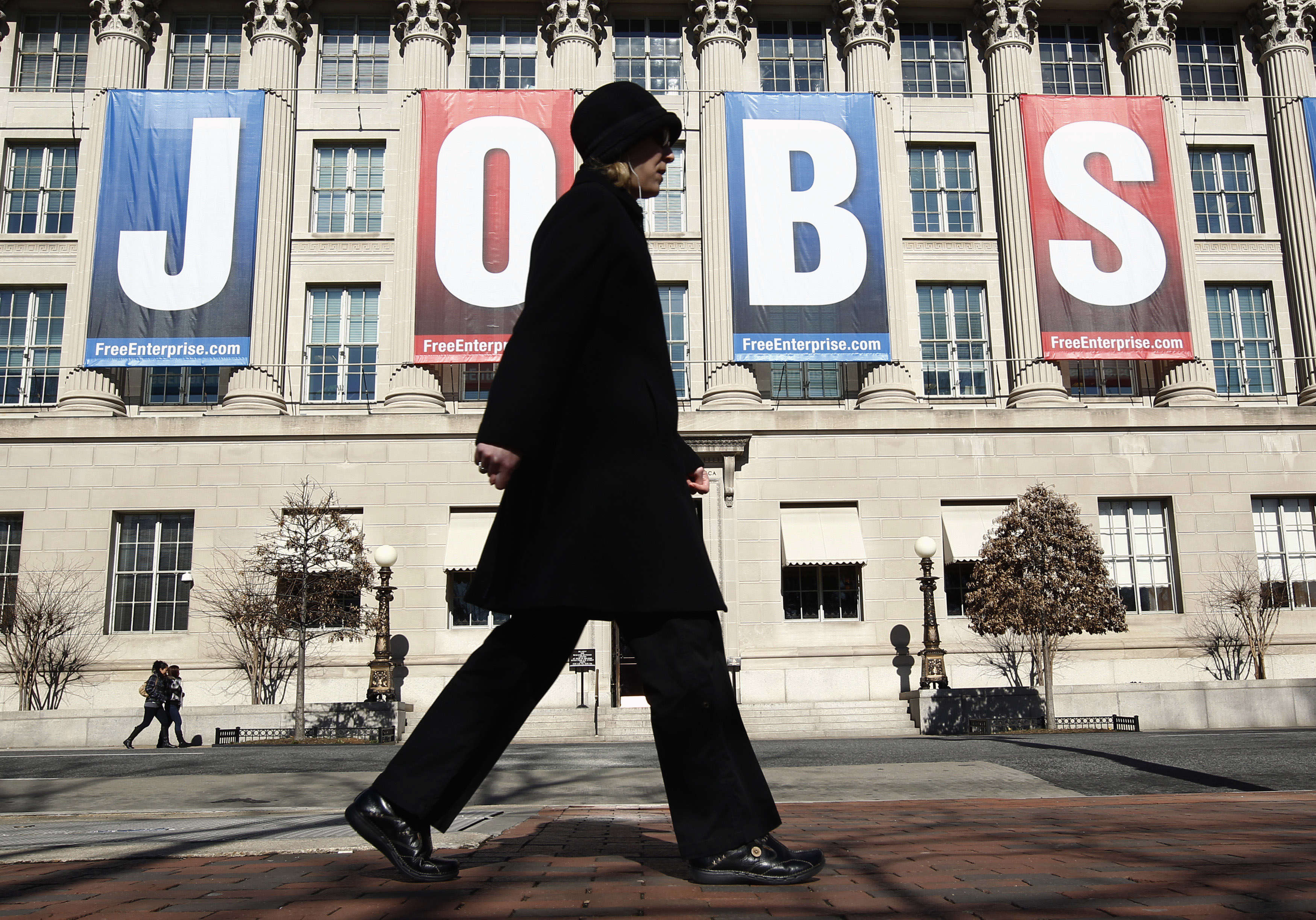 A woman walks past a "Jobs" banner hung above the Chamber of Commerce in Washington February 6, 2012. U.S. President Barack Obama - bolstered by a stronger economic outlook and recent job growth - would win in a match-up against the two leading Republican presidential candidates Mitt Romney and Newt Gingrich, a poll on Monday showed. REUTERS/Kevin Lamarque (UNITED STATES - Tags: BUSINESS EMPLOYMENT) - RTR2XFC1