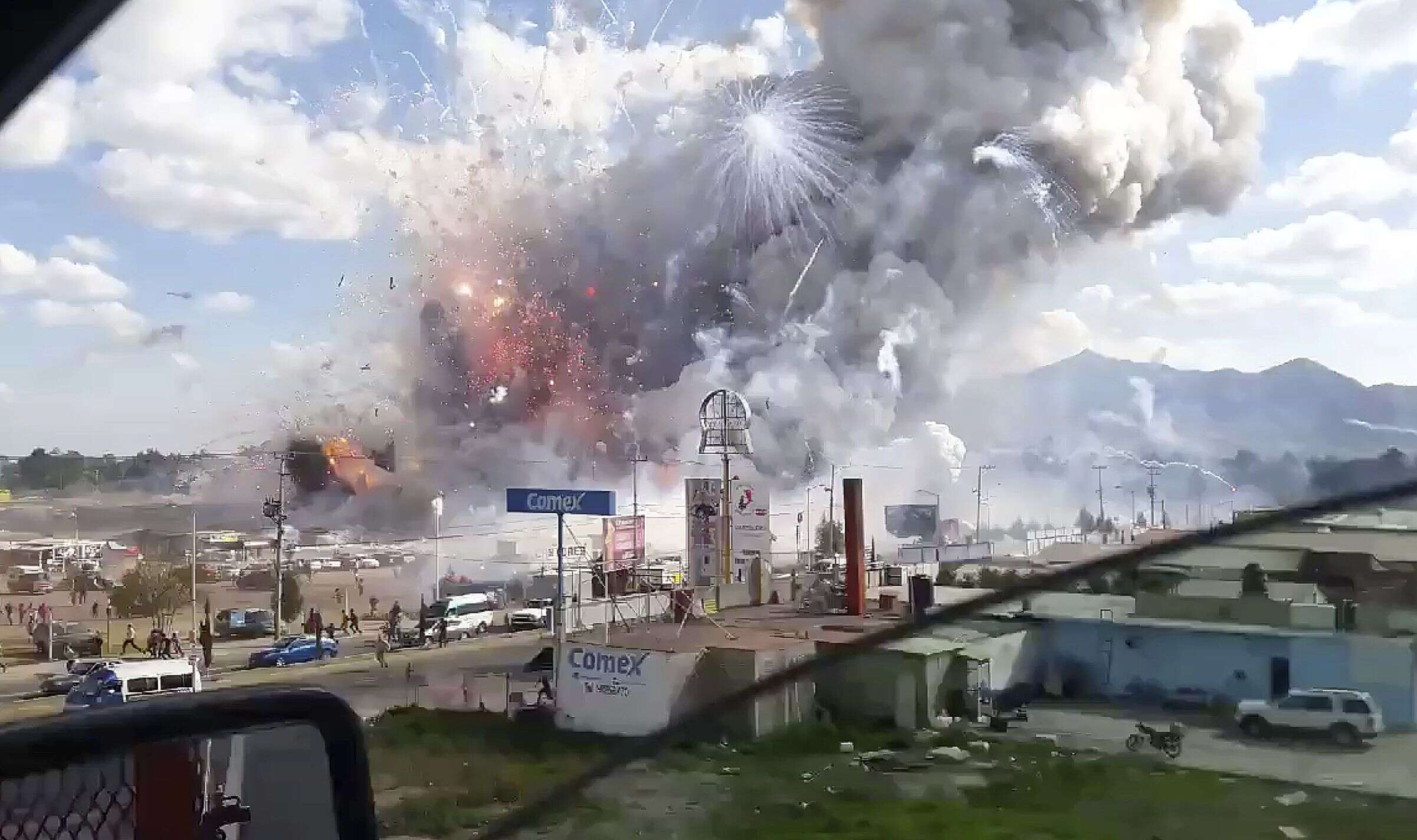 This image made from video recorded from a passing car shows an explosion ripping through the San Pablito fireworks' market in Tultepec, Mexico, Tuesday, Dec. 20, 2016. Sirens wailed and a heavy scent of gunpowder lingered in the air after the afternoon blast at the market, where most of the fireworks stalls were completely leveled. According to the Mexico state prosecutor there are at least 26 dead. (Jose Luis Tolentino via AP)