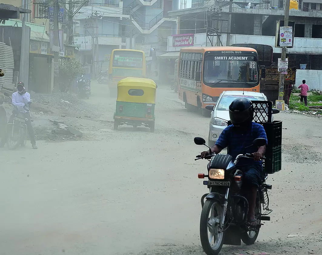 Traffic and a school bus moving through road dust in Bengaluru
