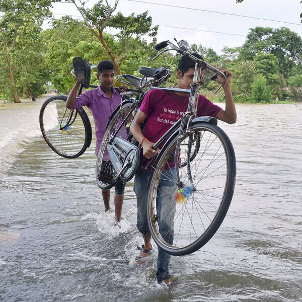 People carry their bicycles as they wade through flood waters