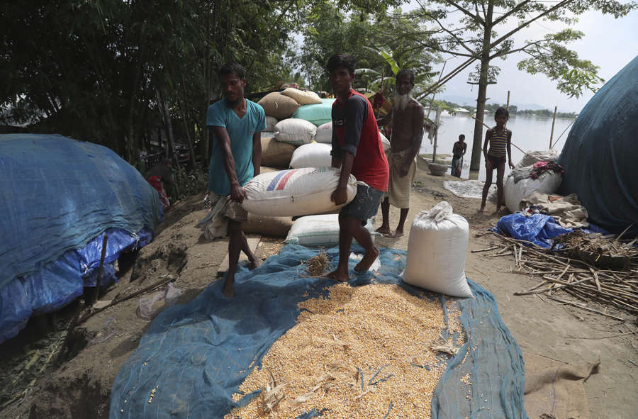 Flood affected villagers carry their grains on an embankment of river ...