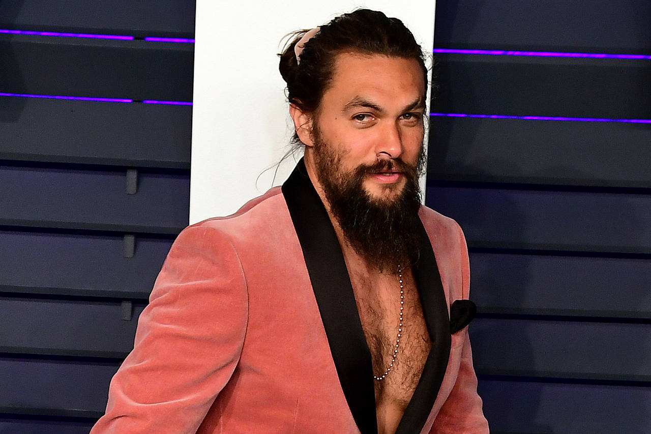 Jason Momoa sporting a pink scrunchie, matching his suit at a red a carpet event