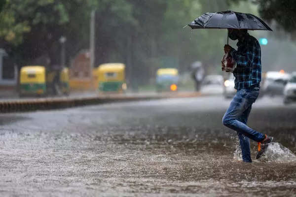 A man crosses a waterlogged street during heavy rain in New Delhi ...