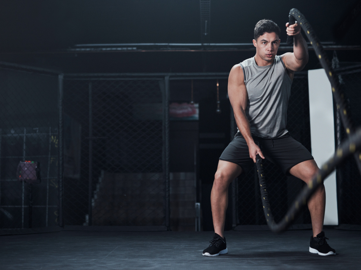  A man in athletic clothing is doing battle rope exercises in a gym and has a look of intense concentration on his face. Injuries from overexertion during exercise can include muscle strains, tendonitis, and stress fractures.