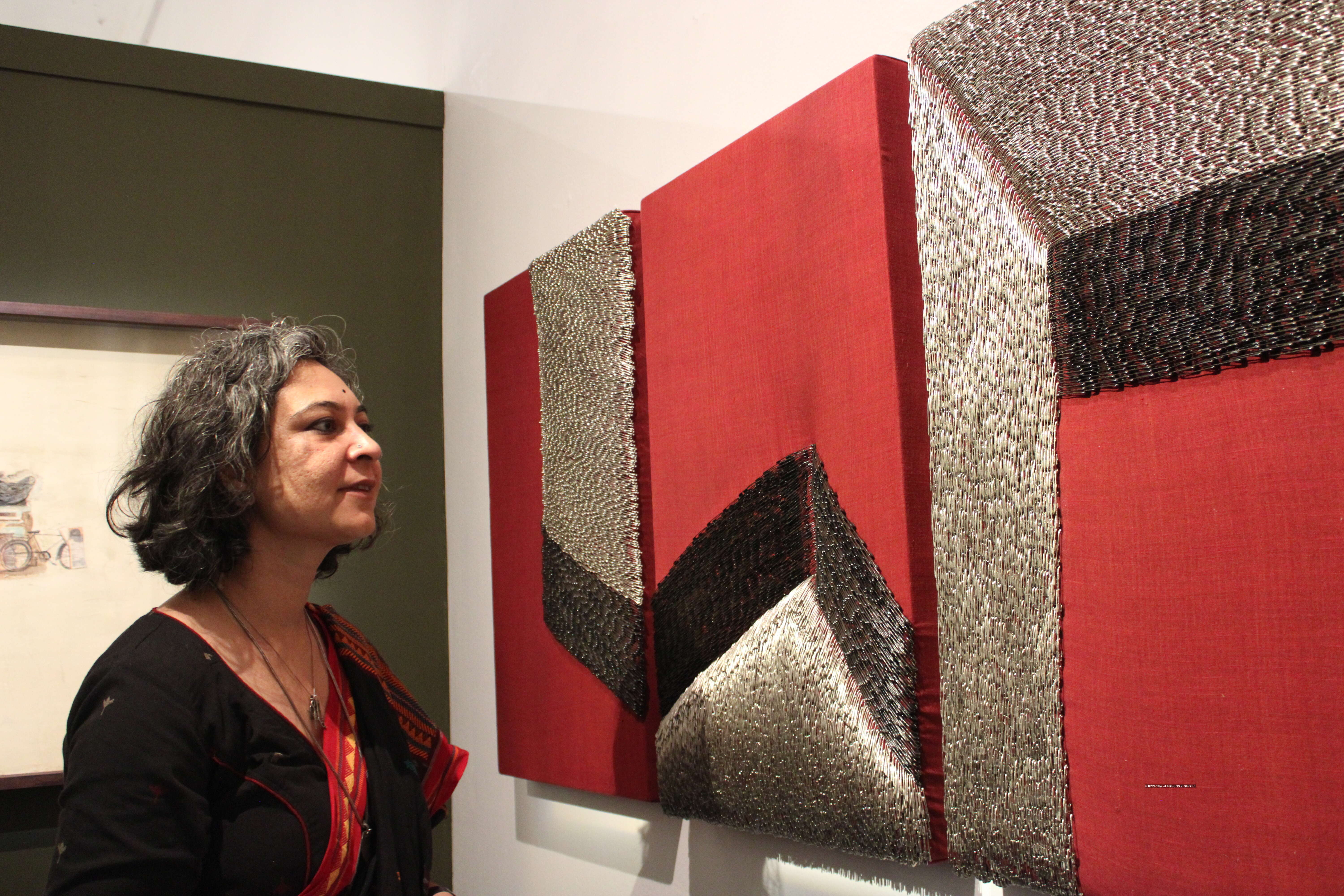 Artist Juhikadevi Bhanjdeo looking at her artwork Skin of Home: aal-dyed panel held together with safetypins