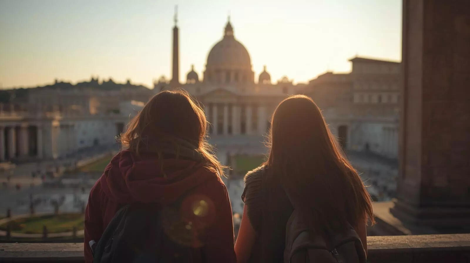 இரண்டு பயணிகள் வாடிகன் நகரத்தை ஆராய்வதை அவர்களின் பின்புறத்திலிருந்து பார்க்க முடியும்