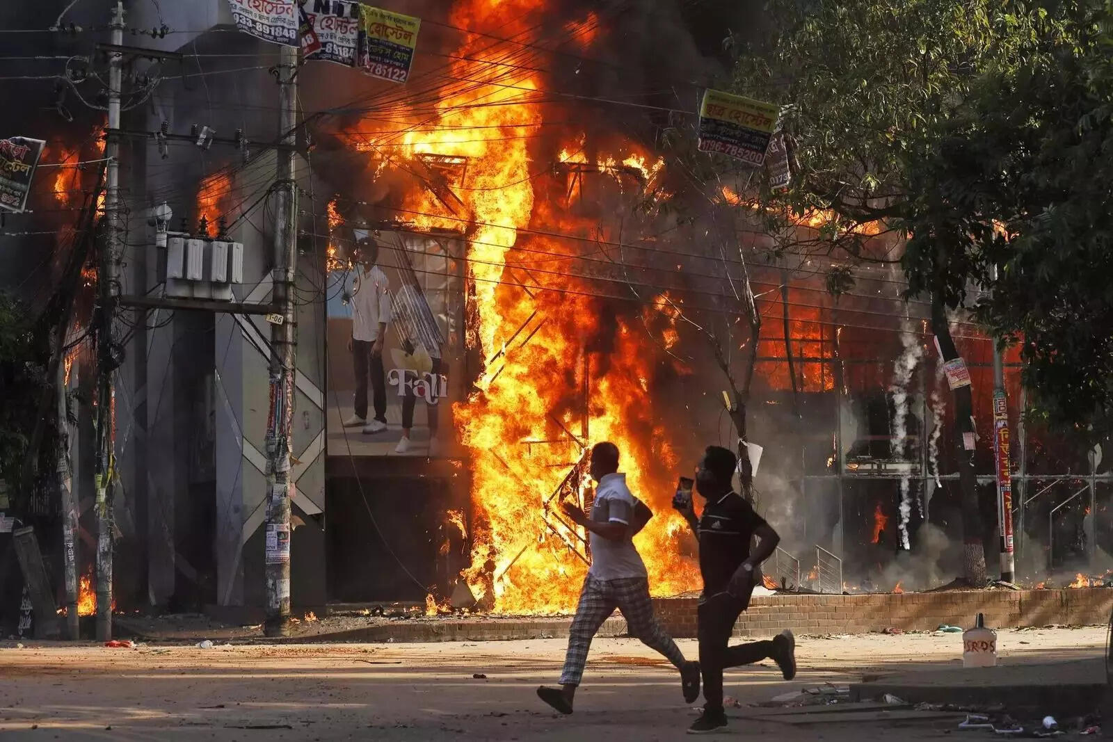 Men run past a shopping center which was set on fire by protesters during a rall....