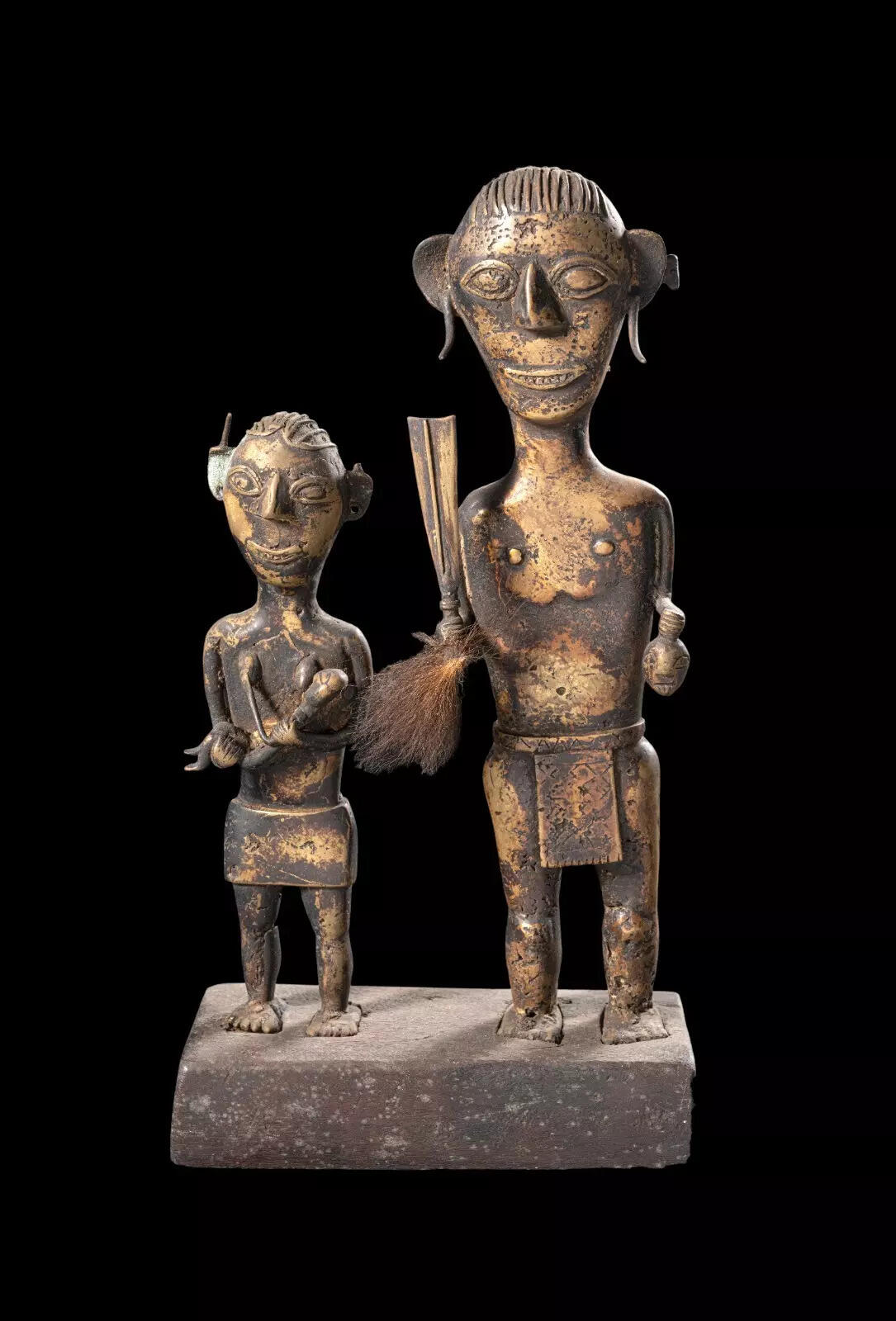 This striking brass sculpture depicts a Konyak Naga couple, standing with poise upon a rectangular wooden pedestal. The male figure, embodying the traditional warrior spirit, holds a Dao in his right hand and a symbolic brass head in the other — powerful emblems of courage and tribal identity