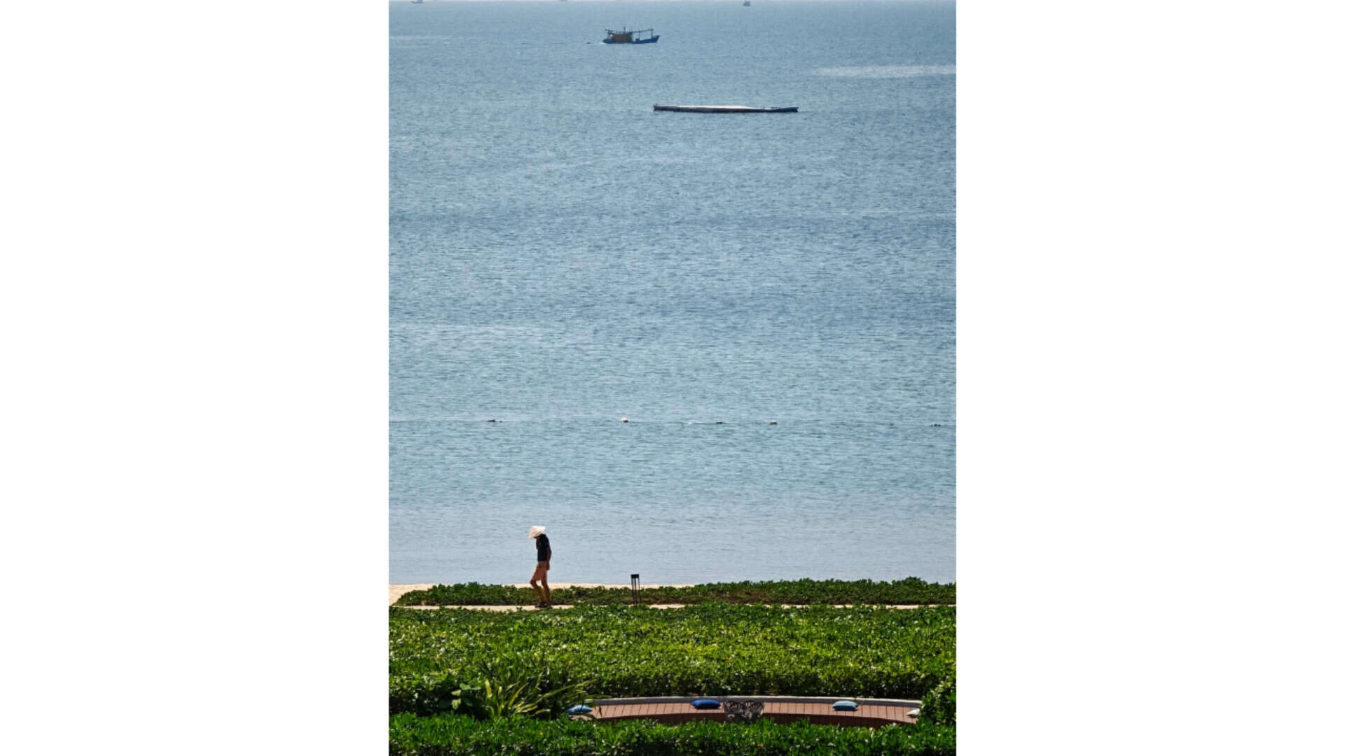 Person walking along beach, boats in distance