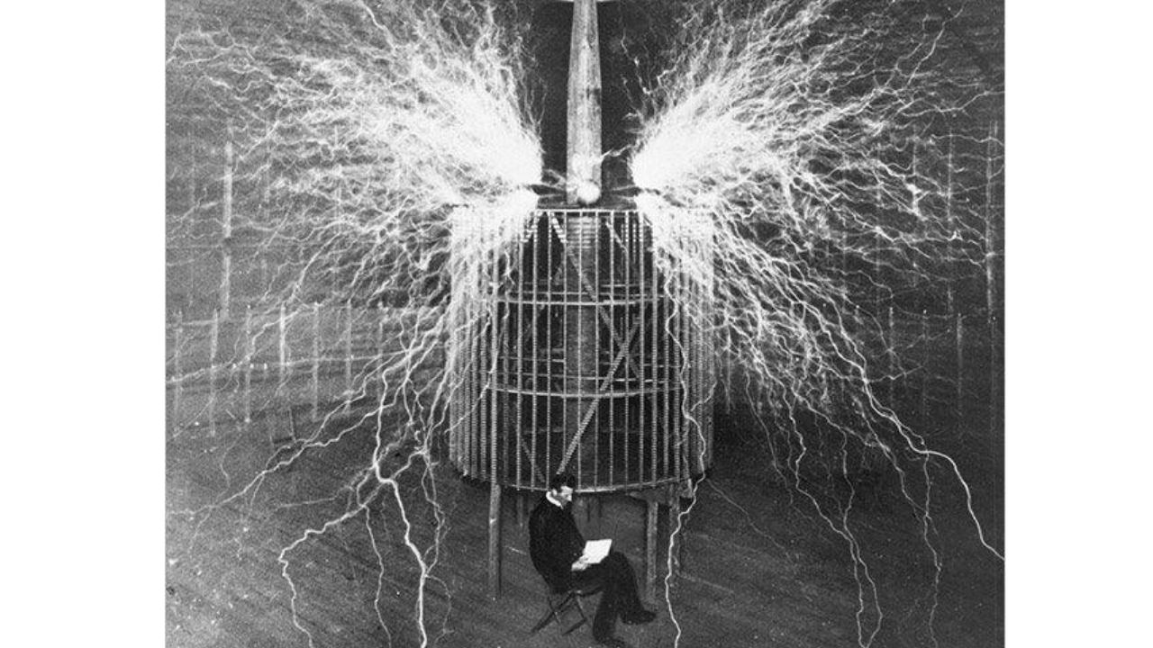 Nikola Tesla seated in his laboratory during high-voltage experiments, surrounded by electrical discharges generated by a Tesla coil, circa 1899.