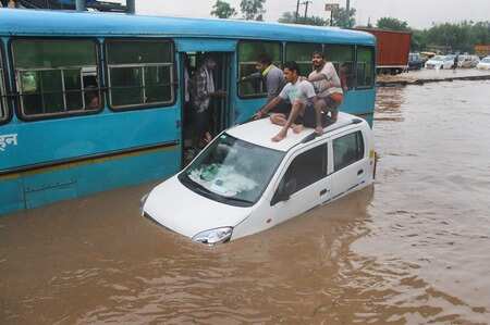 People taking refuge on a submerged car as vehicles ply on waterlogged road in Gurgaon