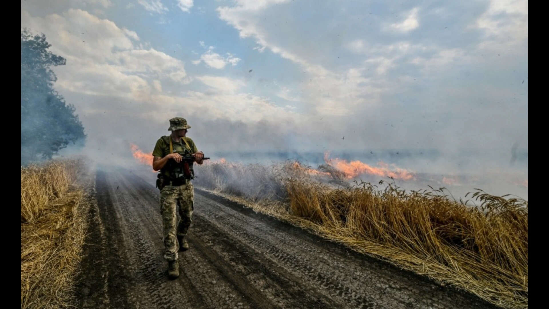 A Ukrainian fighter walks past a burning wheat field (Reuters file photo)