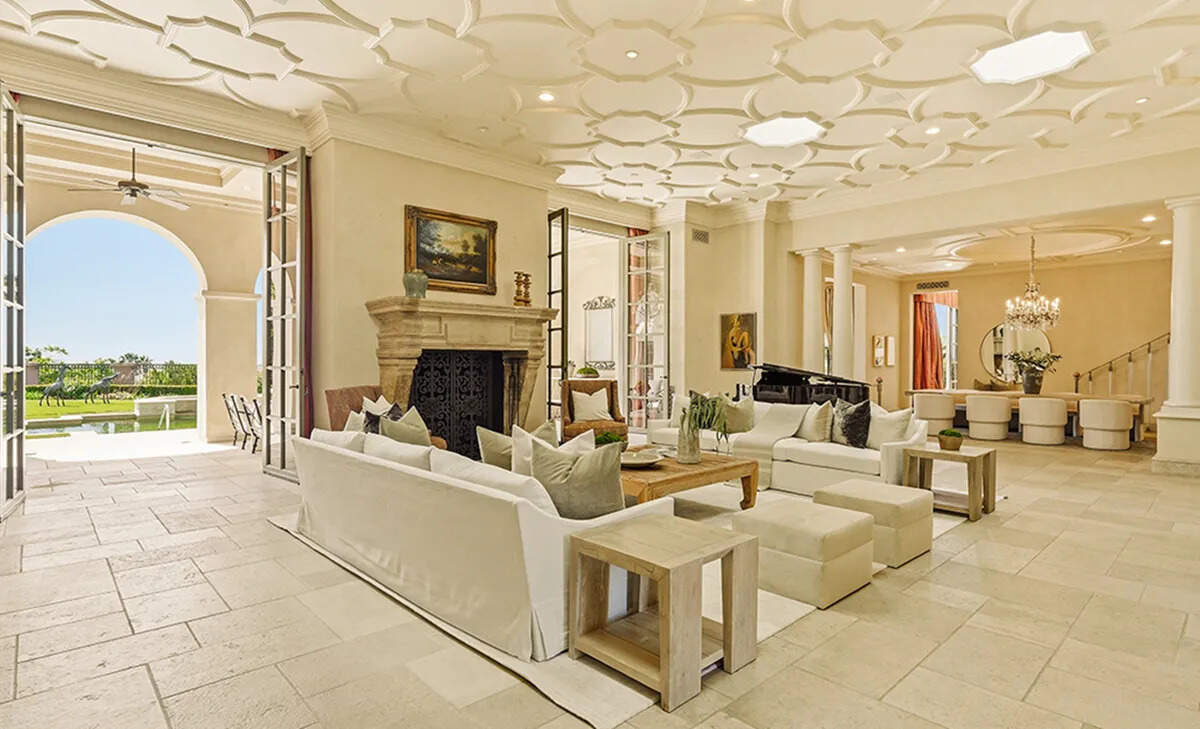 The estate’s expansive living room features a skylit tracery ceiling, carved stone fireplace and French doors opening to a covered loggia.