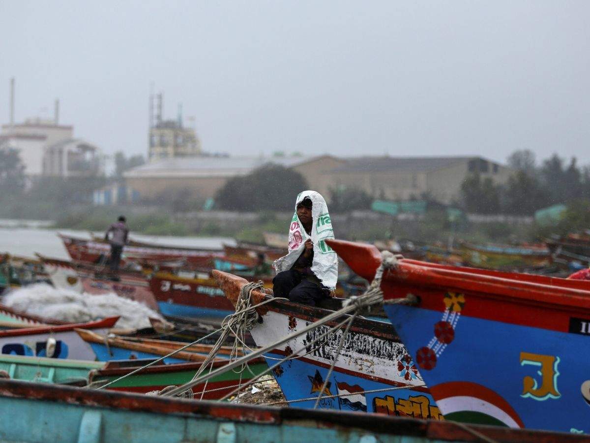 A boy covers himself from rain as he sits on a fishing boat along the shore ahead of Cyclone Vayu in Veraval. (Reuters photo)