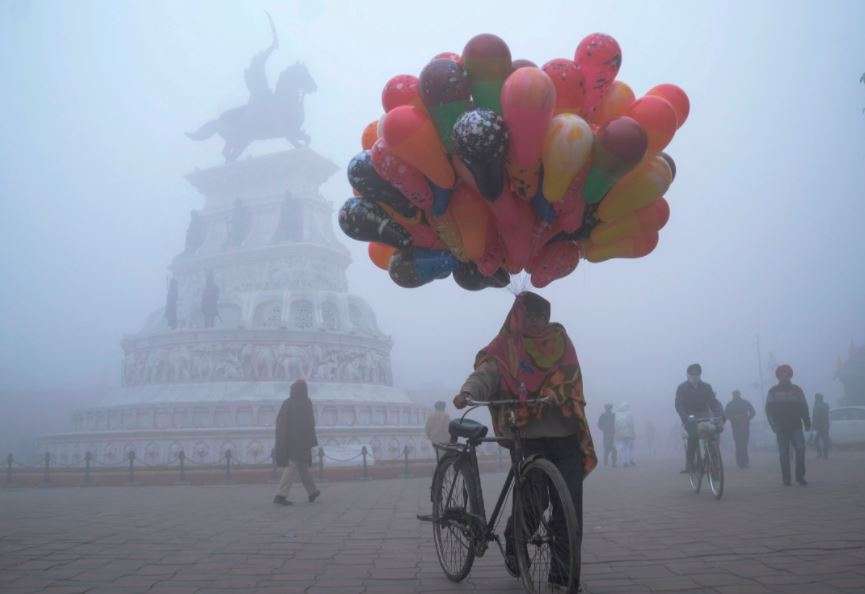 A balloon seller walks along Heritage street amid dense fog on a cold day on New Year's Day, in Amritsar (AFP)
