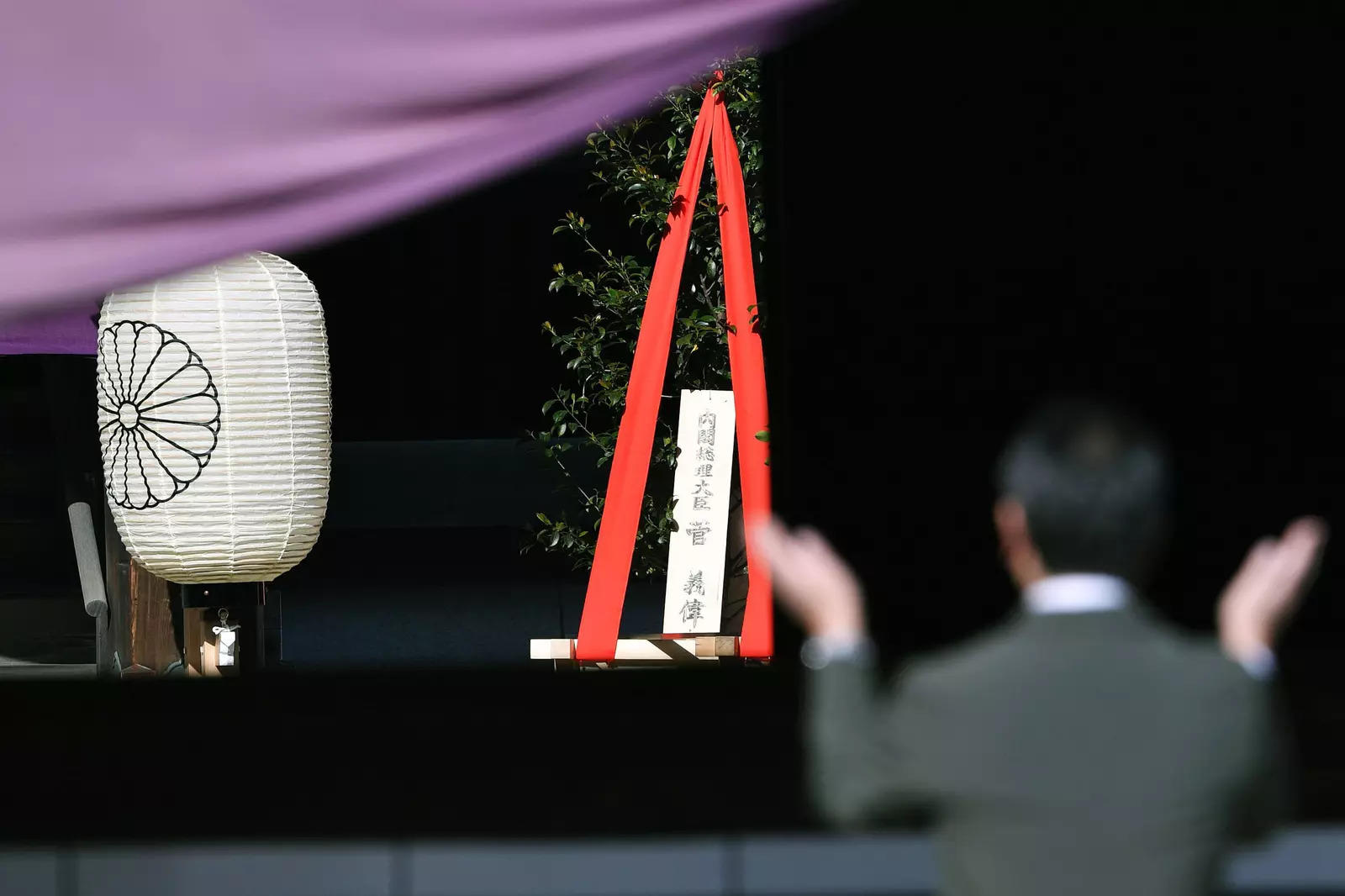 A 'masakaki" tree offering, center, to Yasukuni Shrine by Japanese Prime Minister Yoshihide Suga, is placed as a man prays at the Shinto shrine in Tokyo.