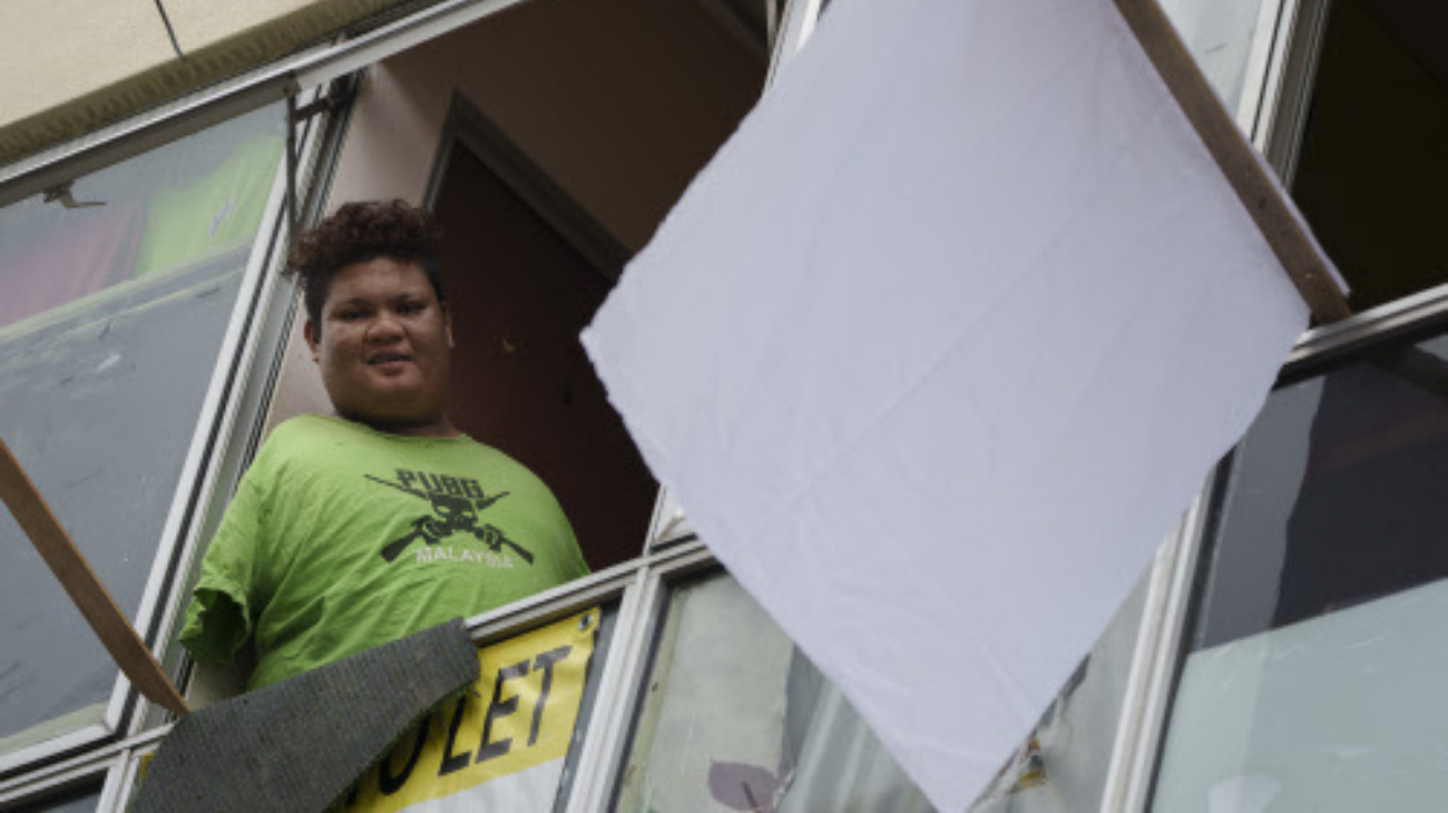 Mohamad Nor Abdullah, born without arms, looks out from a window near a white flag outside the window of his rented room in Kuala Lumpur, Malaysia on July 3, 2021. (Credits: AP)