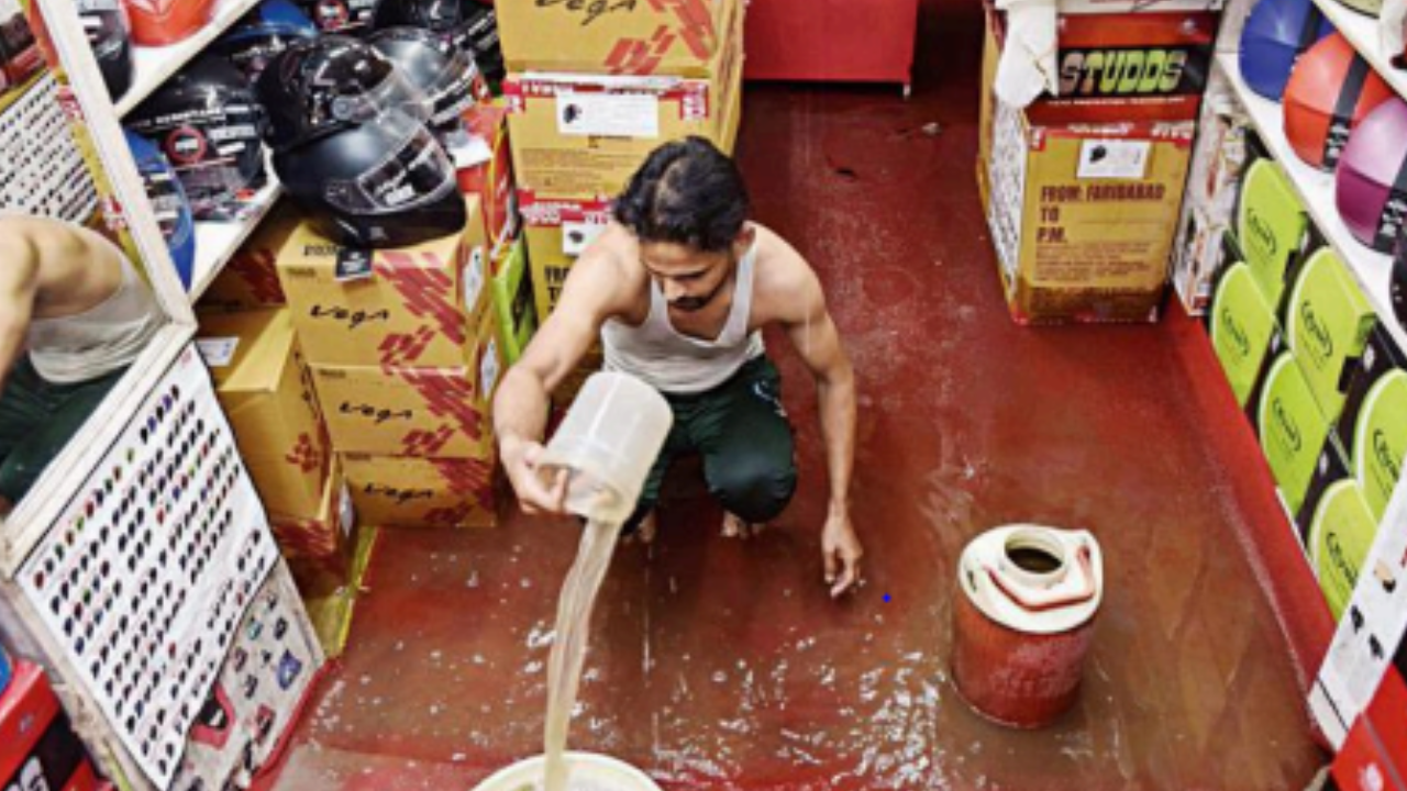 A shopkeeper struggles to keep rainwater out in Laxmi Nagar