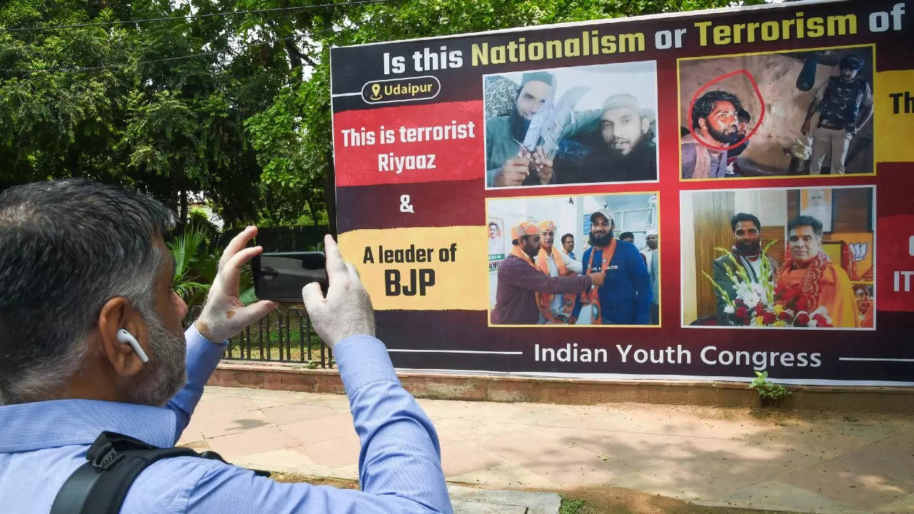 A man clicks picture of a hoarding put up near the Indian Youth Congress office, alleging BJP's connection to Udaipur case accused and arrested Lashkar-e-Taiba (LeT) terrorist Talib Hussain, in New Delhi on Tuesday. PTI photo