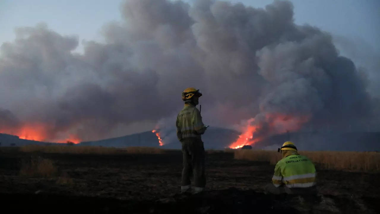 Firefighters guard while the wildfire burns the hills outside Tabara, Zamora, on the second heatwave of the year, in Spain, July 18, 2022 (Reuters)