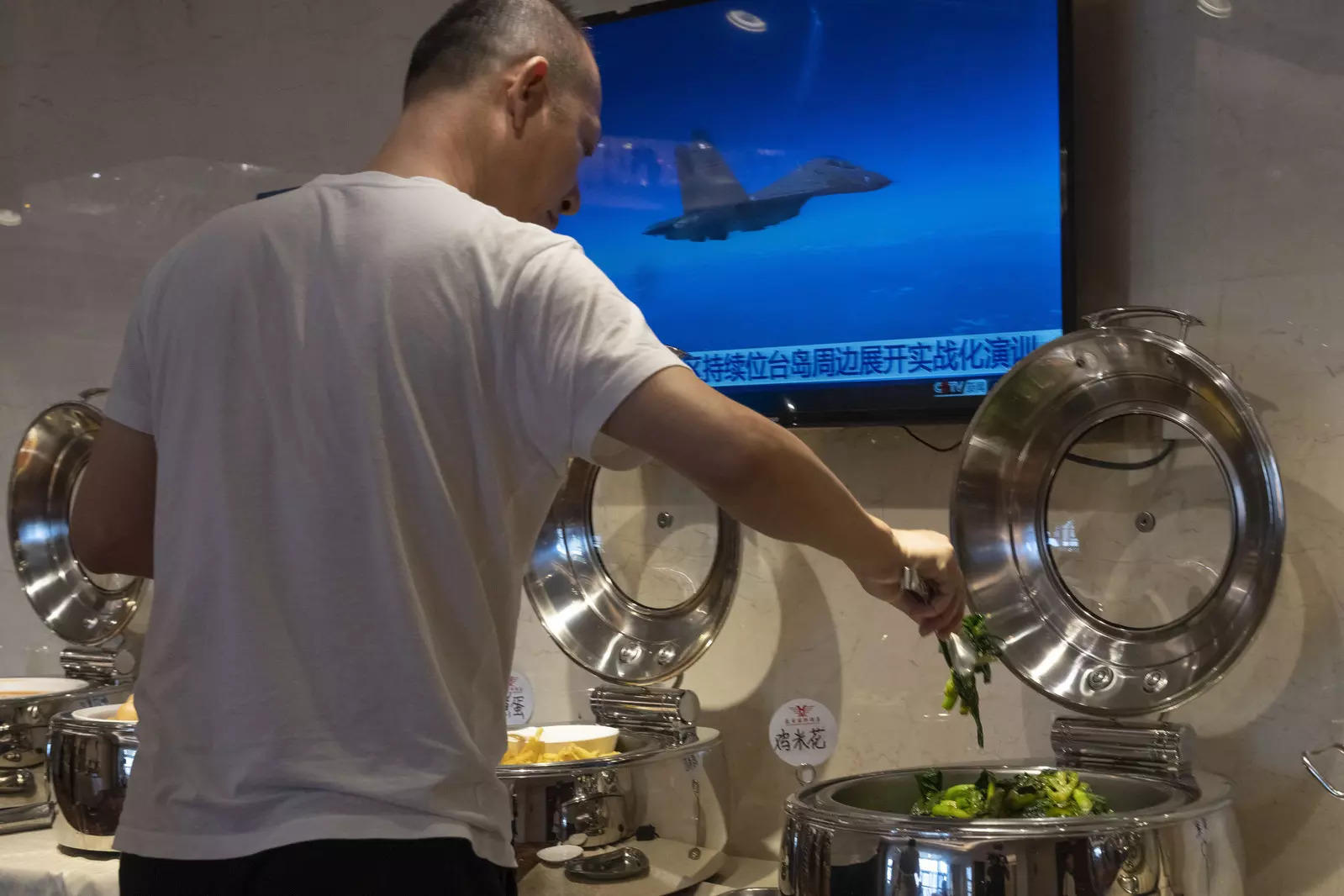 A hotel guests collects food from a breakfast buffet as a news broadcast report on the military exercises, in Pingtan in eastern China's Fujian province on August 6, 2022.  