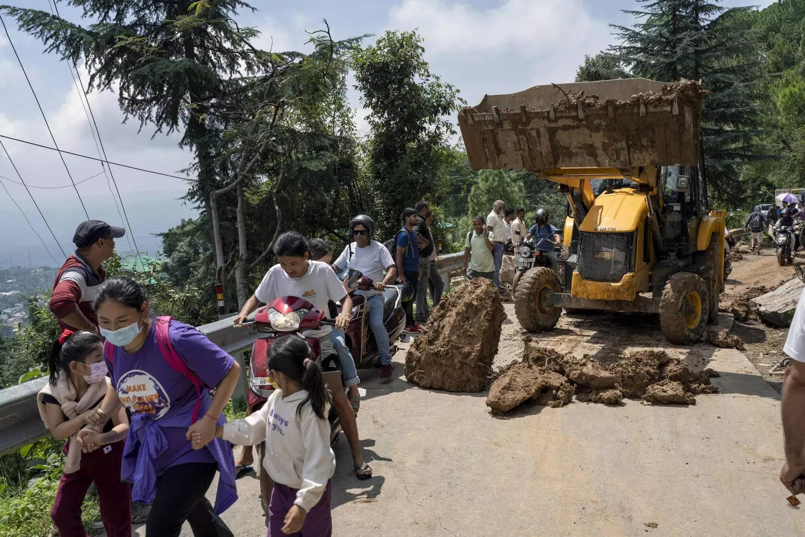 People rush past an earthmover clearing a road of a big rock in Dharamshala due to monsoons.