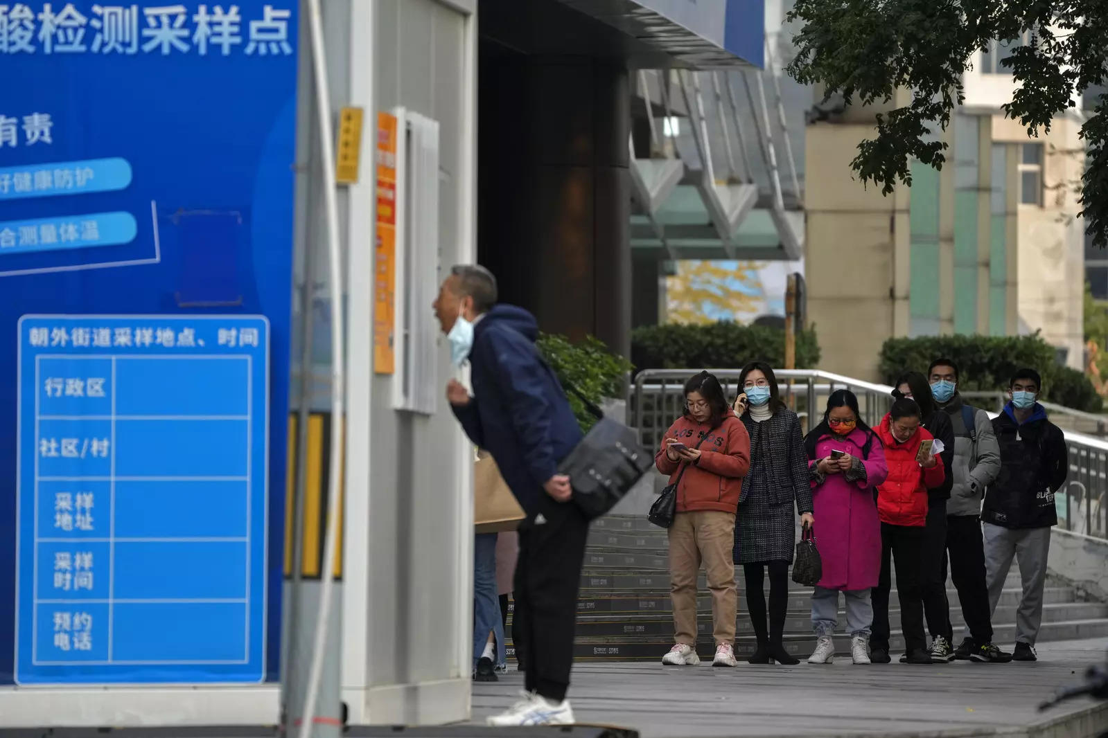 People wait in line for their routine Covid-19 throat swabs at a coronavirus testing site setup along a pedestrian walkway in Beijing