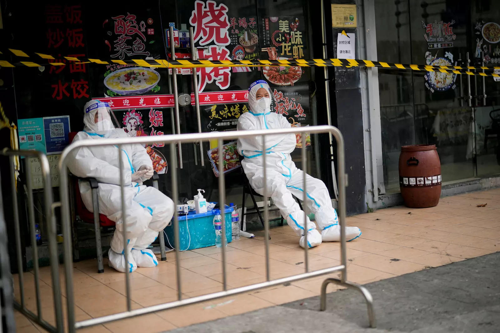 Workers in protective suits keep watch behind a barrier at a sealed restaurant area, following the coronavirus disease  outbreak in Shanghai, China 
