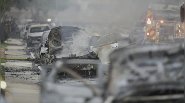 Charred vehicles smolder as emergency crews respond to urban blaze